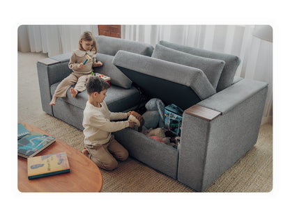 Two children playing beside a charcoal Rezy Smart Sofa with the under-seat hidden storage compartment open and full of toys