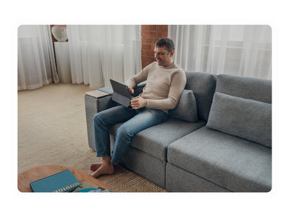 Man sitting on a charcoal sofa using a laptop on the tray table in a living room.